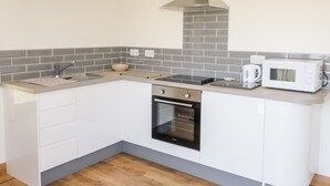 Une cuisine compacte avec des meubles blancs, une hotte de cuisinière en acier inoxydable, un four à micro-ondes et un four encastré.