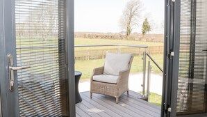 Un balcon avec une chaise en osier et une rambarde en métal, donnant sur un espace verdoyant planté d’arbres.