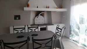 A dining area with a round table, chairs, a white shelf with decorative items, and a window with curtains.