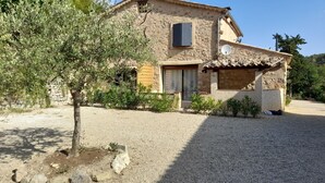 A rustic stone house with a tiled roof, a wooden door, and a gravel driveway.