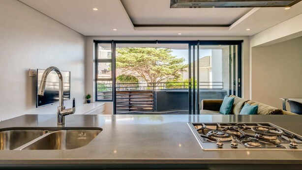 A modern kitchen with a stainless steel sink, a gas stove, and a large window overlooking a balcony. - Conveniently Located Apartment in Green Point (C on S) (Cape Town)