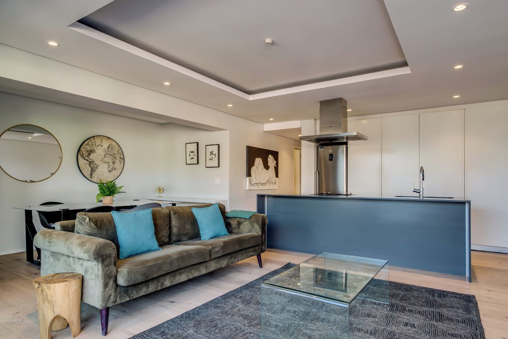 Un salon moderne comprenant un canapé, une table basse et un coin cuisine doté d’un îlot central intégré et d’appareils électroménagers en acier inoxydable.
