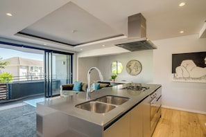 A modern kitchen with a central island, stainless steel appliances, and a large window overlooking a balcony. - Conveniently Located Apartment in Green Point (C on S) (Cape Town)