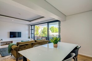 Una sala de estar moderna con un ventanal grande, un televisor de pantalla plana, un sofá, una mesa de comedor y una planta en maceta.