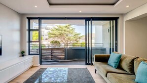 A modern living room with a sofa, a glass door leading to a balcony, and a flat-screen TV on the wall. - Conveniently Located Apartment in Green Point (C on S) (Cape Town)