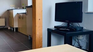 A modern kitchen with a built-in oven, a wooden cabinet, and a black entertainment unit with a flat-screen TV. - Résidence vallée de la Meuse 2 - Blaimont (Blaimont)