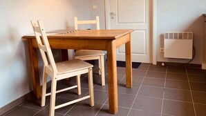A dining area with a wooden table and chairs, a white door, and a wall-mounted heater. - Résidence vallée de la Meuse 2 - Blaimont (Blaimont)