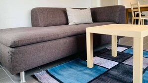 A grey sofa with a light cushion, a wooden table, and a blue and black patterned rug. - Résidence vallée de la Meuse 2 - Blaimont (Blaimont)