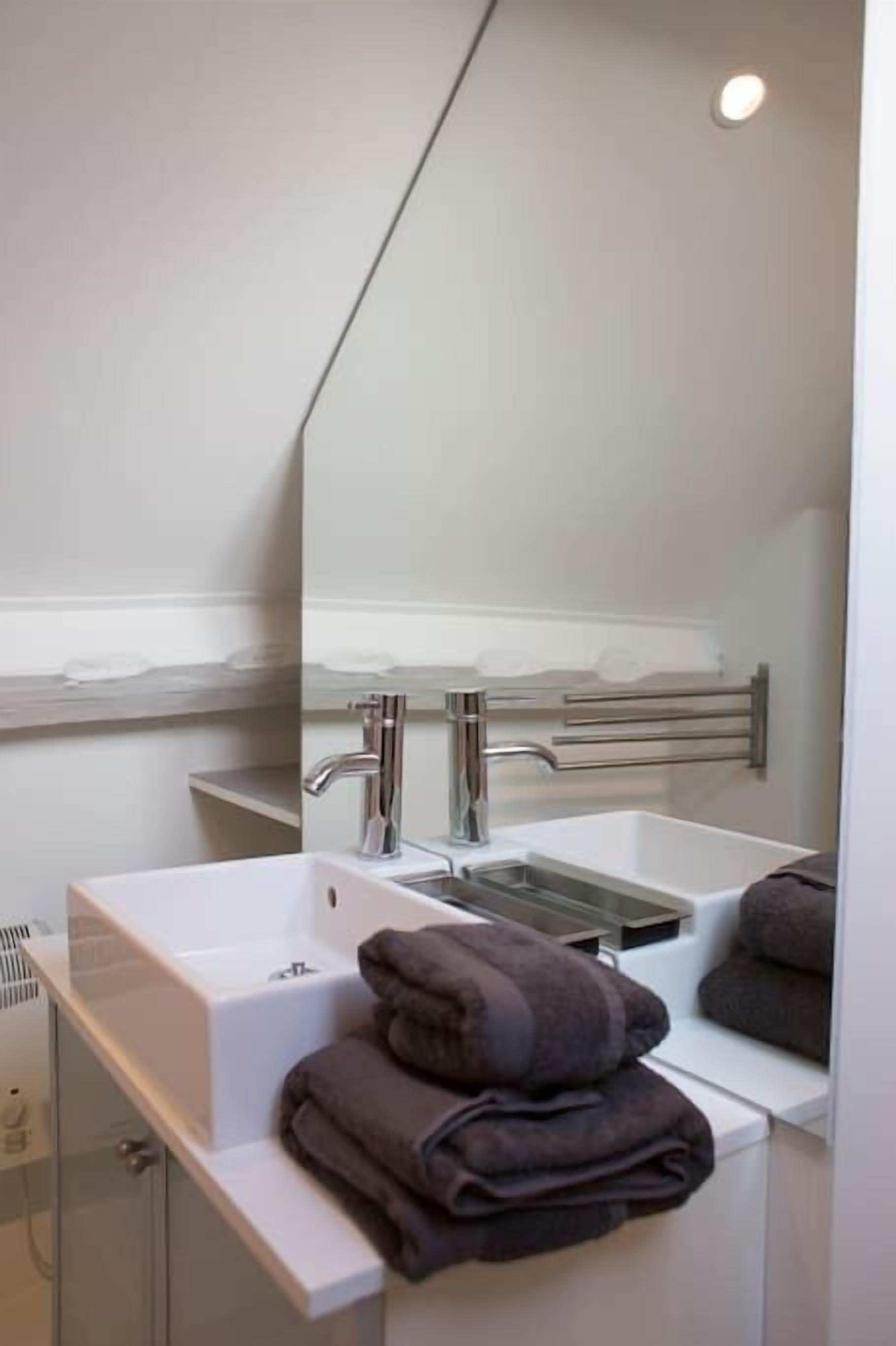 Un baño moderno con lavamanos blanco, un espejo y un perchero para toallas.