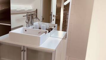 A modern bathroom with a white sink, two cabinets, a large mirror, and a shower area.