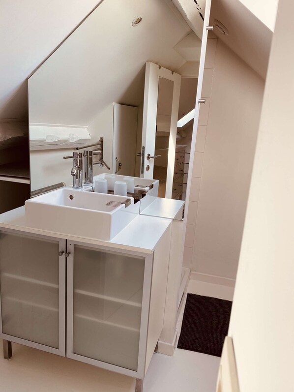 Un baño moderno con un lavamanos blanco, dos armarios, un espejo grande y una zona de ducha.