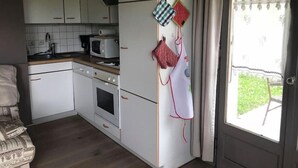A compact kitchen with white cabinets, a microwave, and a stove. There are two hanging kitchen towels and a window with curtains.