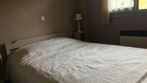 A bedroom with a single bed, a nightstand with a lamp, and a window with curtains.