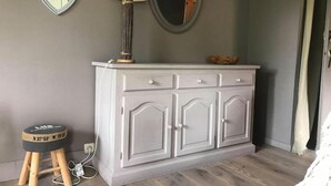 A white cabinet with drawers, a small stool with a compass, a lamp, and two heart-shaped mirrors on the wall.