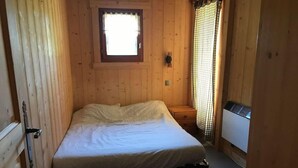 Pieni, puinen huone, jossa on yksi sänky, ikkuna, jossa on verhot, ja patteri.
