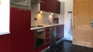 Kompakti keittiö, jossa on punaiset kaapit, ruostumattomasta teräksestä valmistettu uuni, mikroaaltouuni ja kahvinkeitin.