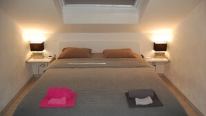 Una cama bien hecha con una colcha gris estampada, dos almohadas marrones y dos lámparas de noche sobre mesitas blancas.