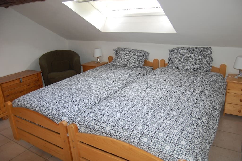 Une chambre dotée d’une lucarne, de deux lits simples avec une literie à motifs, d’une chaise en bois et de tables de chevet avec des lampes.