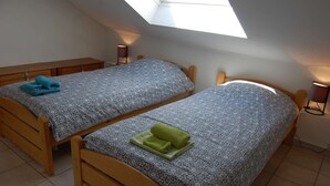 Een slaapkamer met twee houten bedden, elk voorzien van beddengoed en handdoeken met een patroon. Boven de bedden bevindt zich een dakraam, wat zorgt voor natuurlijk licht.