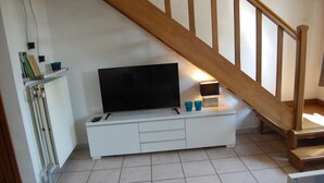 Een woonkamer met een witte entertainmentkast, een flatscreentelevisie en een houten trap.