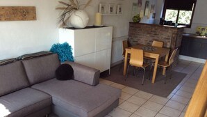 Een moderne woonkamer met een grijze hoekbank, een klein bijzettafeltje, en een eethoek met een houten tafel en stoelen.