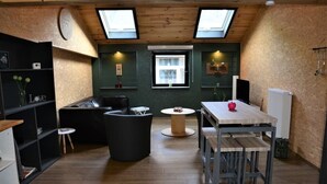 Une cuisine chaleureuse avec un plafond en bois, des fenêtres de toit, une table à manger et un canapé noir.