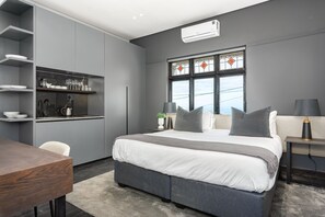 Ein modernes Schlafzimmer mit großem Bett, Nachttischen, einem Schreibtisch und einer integrierten Küchenzeile.