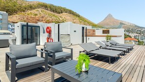 Eine Dachterrasse mit Liegestühlen und einem Tisch, mit Blick auf eine gebirgige Landschaft.