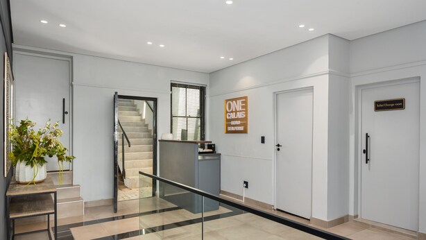 A modern hotel lobby with a staircase, a reception desk, a sign reading "ONE CALAIS," and a sign for the "Toilet/Change room." - One Calais | Corner Studio with Ocean Views (Cape Town)