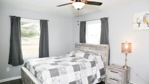 Een slaapkamer met een bed, nachtkastje, lamp en plafondventilator.