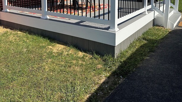 Een terras bij een woning met een witte balustrade, een patio tafel en een blauwe parasol.