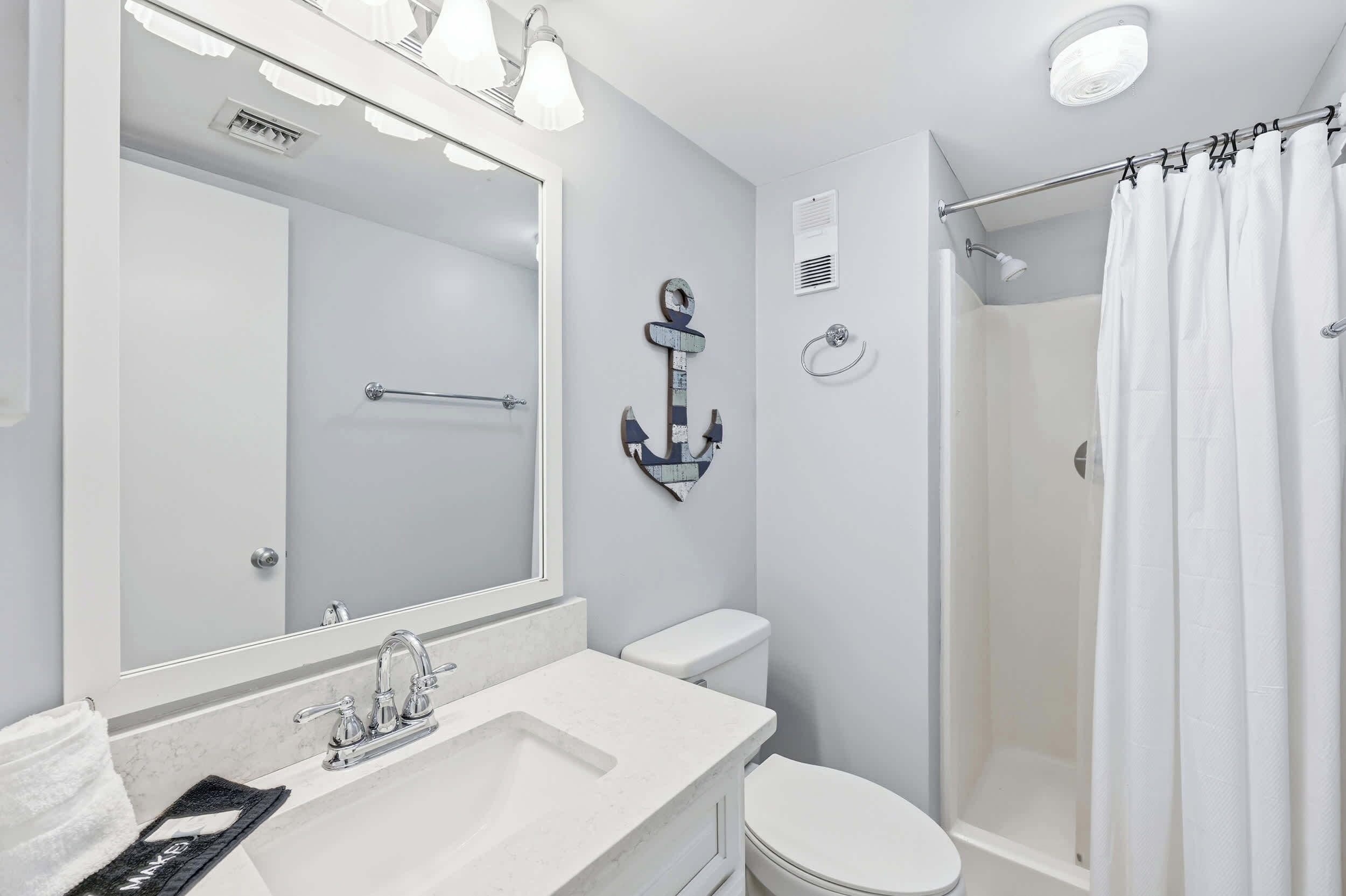 A bathroom with a sink, toilet, shower, and a mirror with lights.