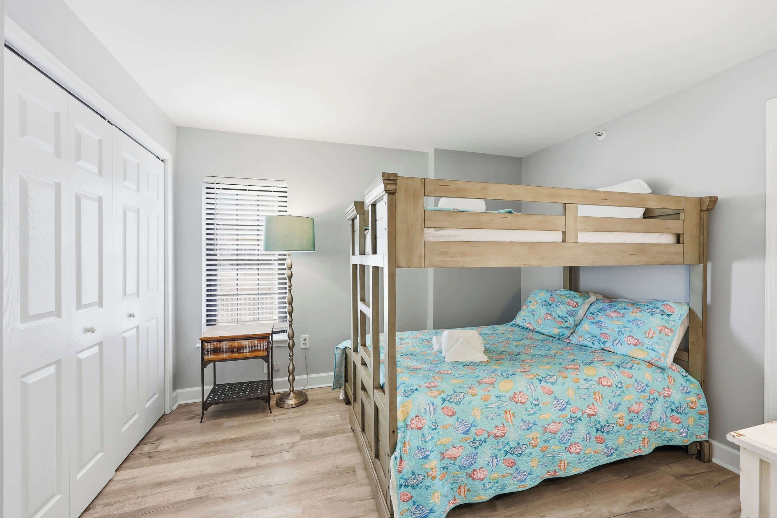 A bedroom with a bunk bed, a bedside table, a lamp, and a window with blinds.