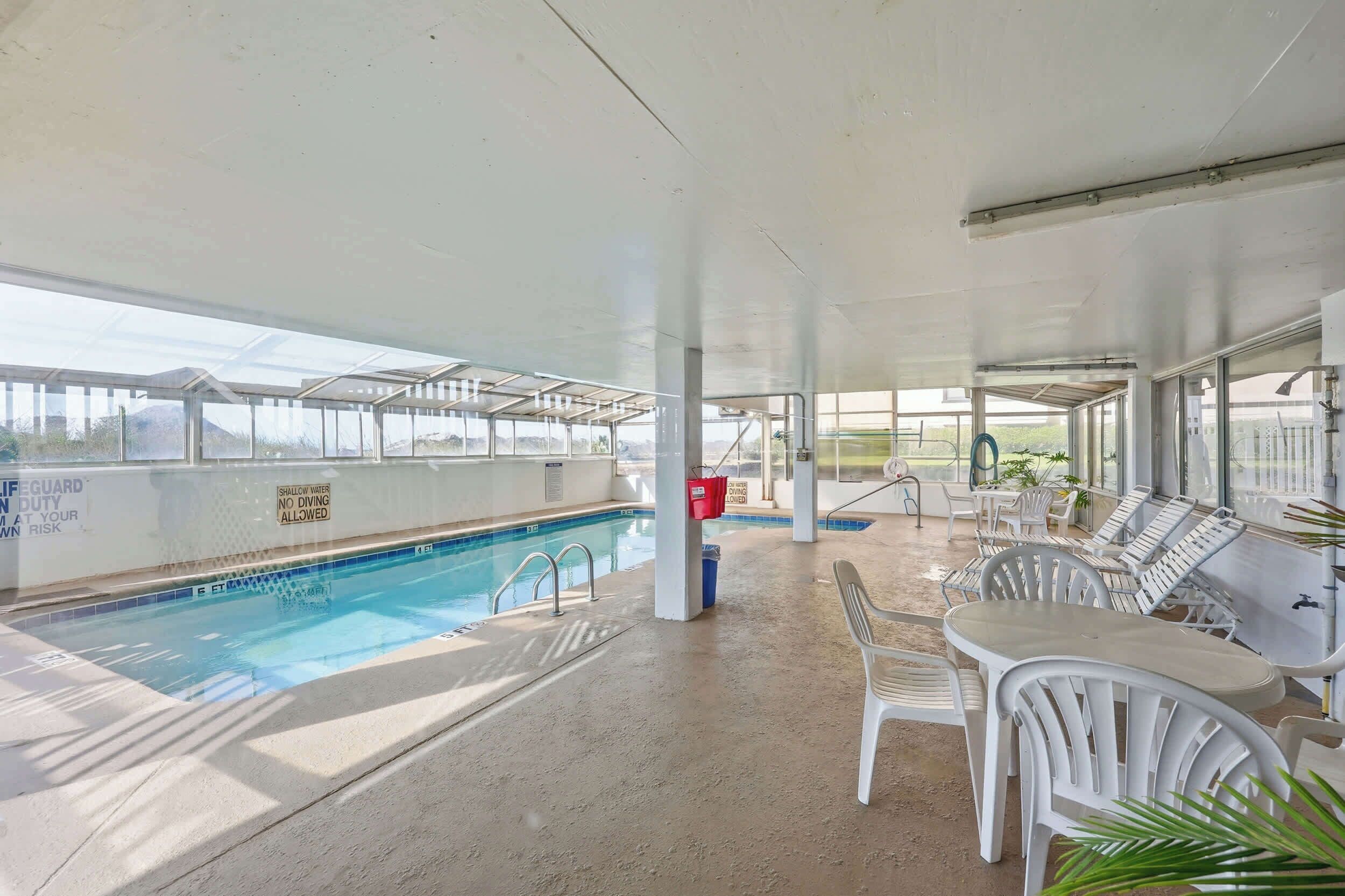 An indoor pool area with clear glass walls, a pool, and lounge chairs.