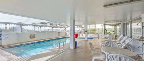 An indoor pool area with clear glass walls, a pool, and lounge chairs.