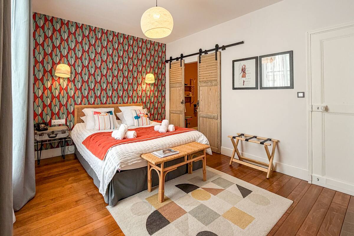 A bedroom with a bed, bedside table, lamp, bench, and a patterned rug.