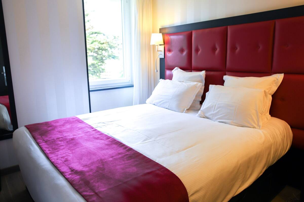 A hotel room with a bed, a window, and a red headboard.
