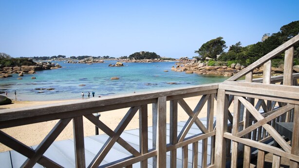 A wooden deck overlooking a beach with clear water and rocky outcrops.