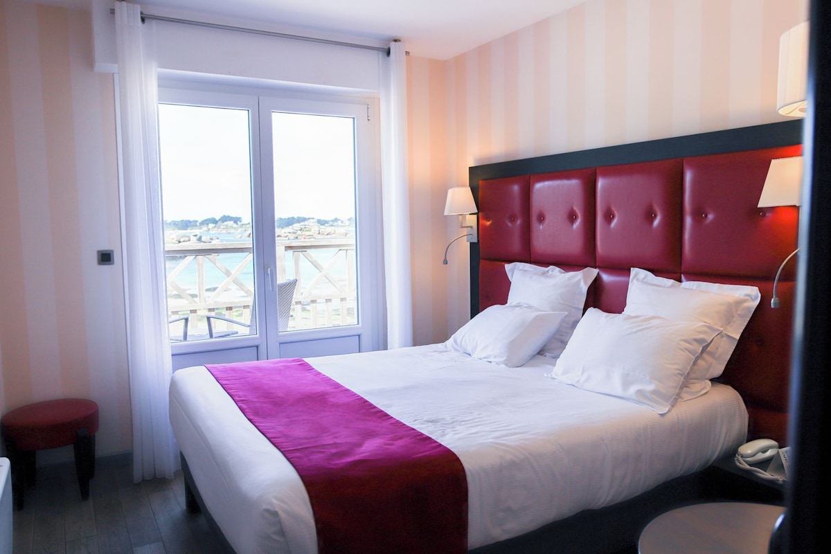 Una habitación de hotel con cama, mesita de noche, lámpara y vista al mar.