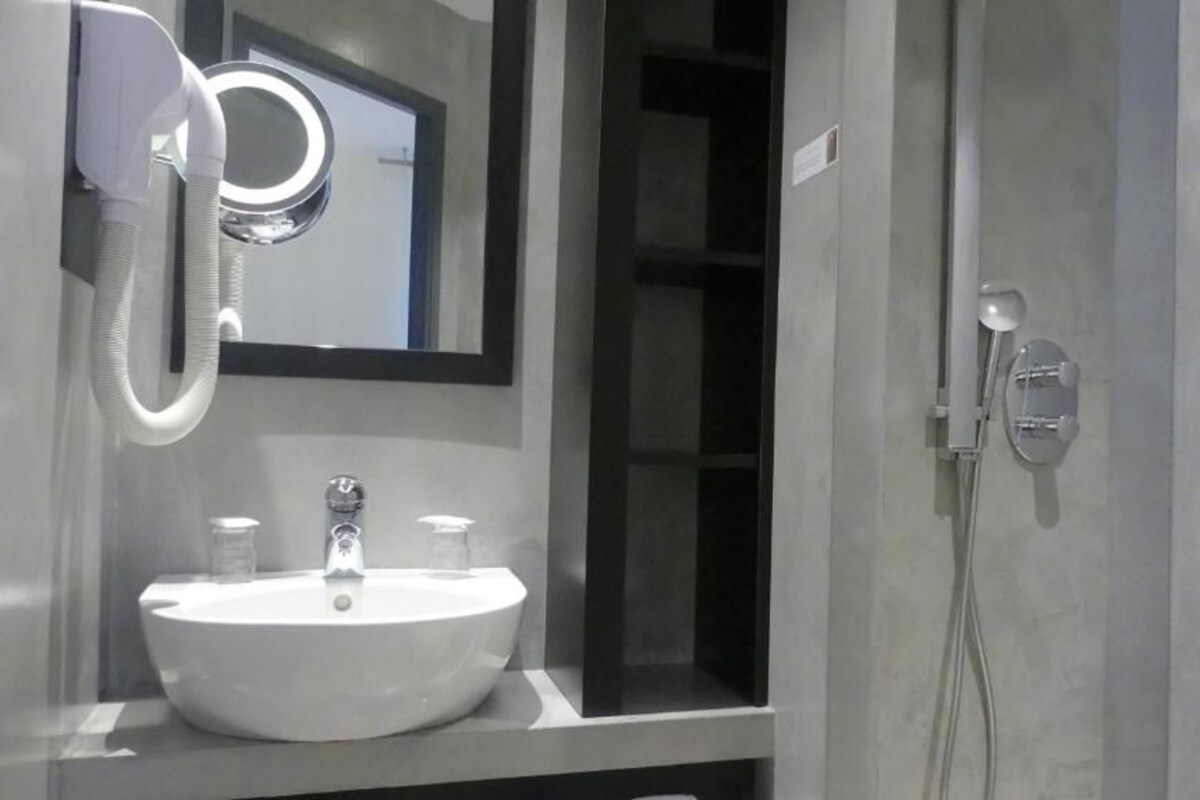Une salle de bain avec un lavabo blanc, un miroir, un sèche-cheveux et une douchette à main.