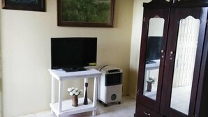 Une chambre à coucher avec un lit, un téléviseur posé sur un meuble blanc, un radiateur et une armoire.