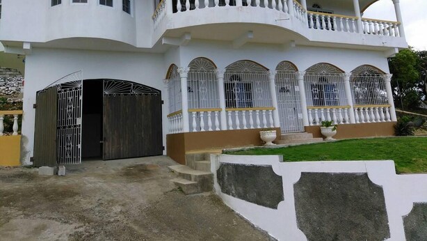 Une maison à deux étages dotée d’un balcon, d’une entrée sécurisée par un portail et d’un petit jardin.