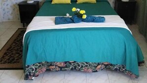 Une chambre à coucher avec un lit, deux tables de chevet, un papier peint à motifs floraux et une couvre-lit verte et blanche.