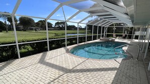 Ein überdachter Pool mit Backsteinböden, umgeben von einem weißen Metallrahmen, mit Blick auf eine grüne Landschaft im Hintergrund.