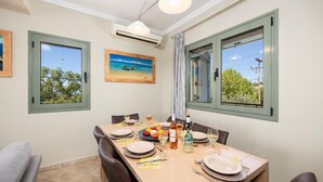 Zona pranzo con tavolo apparecchiato per quattro persone, un quadro e vista su alberi e linee elettriche dalle finestre.