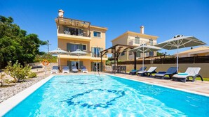 Una piscina con lettini e ombrelloni, circondata da edifici con balconi.