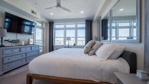A modern bedroom with a large bed, a ceiling fan, a TV, and a dresser.