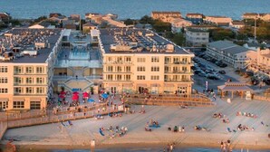 A coastal hotel with multiple floors, a beach area with sun loungers, and a parking lot.