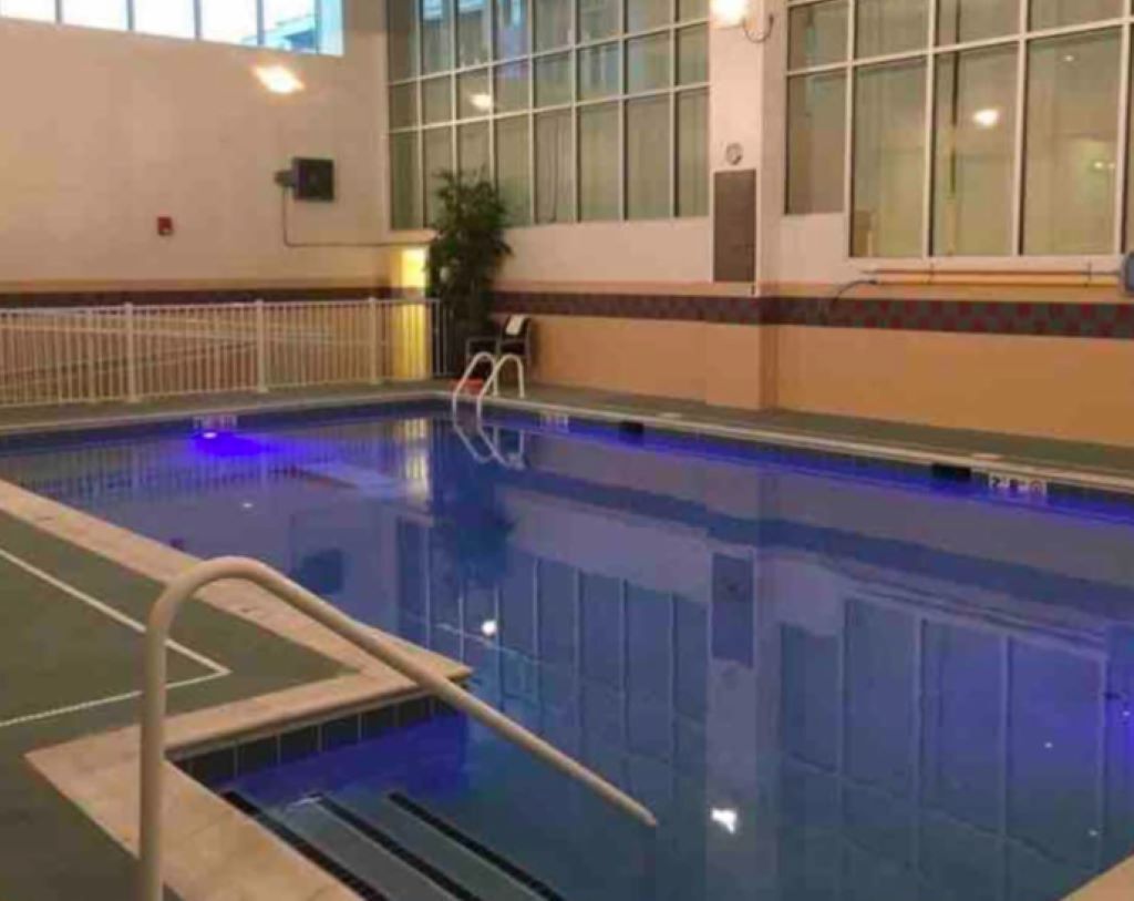 Ein Hallenbad mit klarem Wasser, einem Sprungbrett und einem weißen Sicherheitszaun.