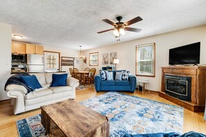 A living room with a beige sofa, a blue sofa, a wooden coffee table, a fireplace, and a ceiling fan.